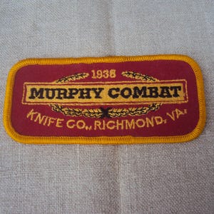 Puede incluir: Un parche bordado rojo y dorado con el texto "Murphy Combat Knife Co., Richmond, VA" y el año "1938" sobre el texto.