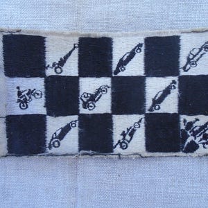 Pode incluir: Um patch retangular com um padrão xadrez preto e branco. Os quadrados apresentam imagens bordadas de motocicletas e carros de corrida em preto. O patch tem uma borda bege e é provavelmente para uma jaqueta ou bolsa.