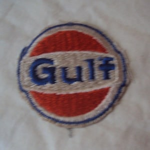 Puede incluir: Un parche bordado vintage con fondo blanco y un círculo rojo y blanco con la palabra "Gulf" en letras azules.