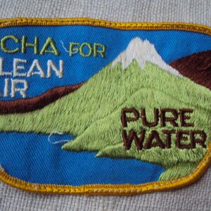 Könnte beinhalten: Ein blauer und gelber gestickter Aufnäher mit einer Bergszene und dem Text "NCHA FOR CLEAN AIR PURE WATER".