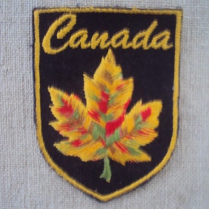 May include: A black felt patch with a yellow embroidered maple leaf and the word "Canada" in yellow lettering.