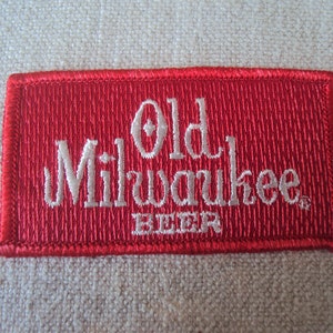 Peut inclure: Écusson brodé rouge avec du texte blanc qui dit "Old Milwaukee Beer".