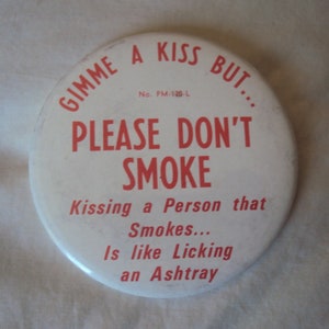 Könnte beinhalten: Ein runder, weißer Button mit rotem Text. Der Text lautet: "Gimme a kiss but... PLEASE DON'T SMOKE. Jemanden küssen, der raucht... ist wie einen Aschenbecher lecken."