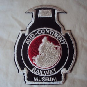 May include: A black and white embroidered patch with a red circle in the centre. The circle has a white silhouette of a train engine. The text "MID-CONTINENT RAILWAY MUSEUM" is embroidered around the circle.