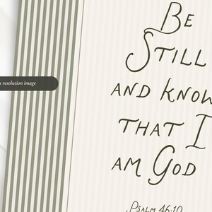 May include: A cream-colored print with the words "Be Still and Know That I Am God" in elegant script. The text is in dark brown, with "Psalm 46:10" at the bottom. A section with vertical stripes in olive green and white is on the left.