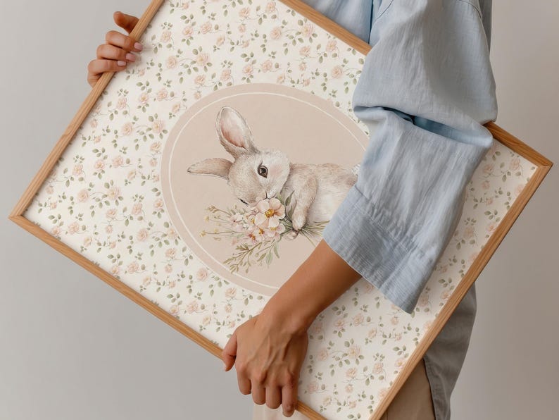 K&ouml;nnte beinhalten: Ein gerahmter Druck mit einer Aquarellillustration eines Hasen und Blumen. Der Hintergrund hat ein Blumenmuster mit kleinen rosa Rosen. Der Rahmen ist aus hellfarbenem Holz.