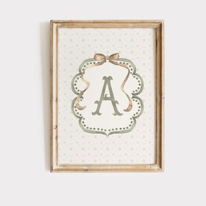May include: Framed wall art featuring the letter "A" in a decorative, ornate frame. The letter is in a soft green hue, surrounded by a scalloped border with a bow at the top. The background has a subtle floral pattern, all within a wooden frame.