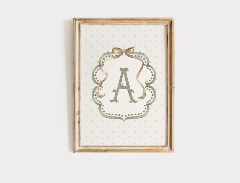 May include: Framed wall art featuring the letter "A" in a decorative, ornate frame. The letter is in a soft green hue, surrounded by a scalloped border with a bow at the top. The background has a subtle floral pattern, all within a wooden frame.