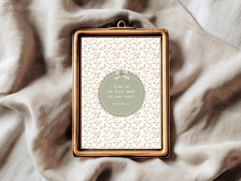 Op de afbeelding: Een rechthoekige, goudkleurige ingelijste print met een bloemenpatroon achtergrond. De print heeft een cirkelvormig ontwerp met de tekst "Trust in the Lord with all your heart." Het frame heeft een kleine lus aan de bovenkant om op te hangen.