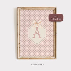 Puede incluir: Arte de pared enmarcado con un fondo de patr&oacute;n geom&eacute;trico rosa y blanco. La letra "A" rosa claro est&aacute; centrada en una forma decorativa crema, adornada con un lazo. El texto "A-Z INCLUDED" est&aacute; en un rect&aacute;ngulo marr&oacute;n.