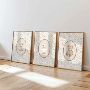 Op de afbeelding: Drie ingelijste kunstdrukken met aquarel illustraties van een lam, een gans en een teddybeer. Elke afbeelding staat in een ovale lijst tegen een bloemenachtergrond. De lijsten zijn lichtbruin.