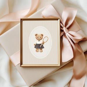 K&ouml;nnte beinhalten: Ein gerahmter Aquarelldruck eines Teddyb&auml;ren in Tennisbekleidung, der einen Schl&auml;ger h&auml;lt. Der Druck befindet sich vor einem cremefarbenen Hintergrund mit vertikalen Streifen, in einem goldenen Rahmen. Der Rahmen liegt auf einer Geschenkbox mit Pfirsichfarbenem Band.