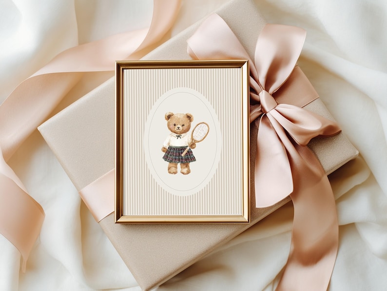 K&ouml;nnte beinhalten: Ein gerahmter Aquarelldruck eines Teddyb&auml;ren in Tennisbekleidung, der einen Schl&auml;ger h&auml;lt. Der Druck befindet sich vor einem cremefarbenen Hintergrund mit vertikalen Streifen, in einem goldenen Rahmen. Der Rahmen liegt auf einer Geschenkbox mit Pfirsichfarbenem Band.