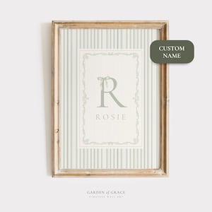 Peut inclure: Tableau encadré avec un fond à rayures vertes et blanches. L'œuvre présente la lettre "R" verte clair avec un nœud, le nom "Rosie" et des bordures décoratives. Le cadre est de couleur marron clair. Le texte "CUSTOM NAME" est dans un rectangle vert arrondi.