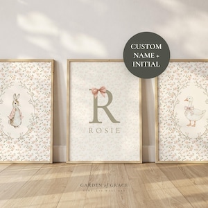 May include: Three framed nursery art prints. One features a bunny, another a duck, and the centre print has a letter "R" and the name "Rosie". All prints have a floral background and are in wooden frames.