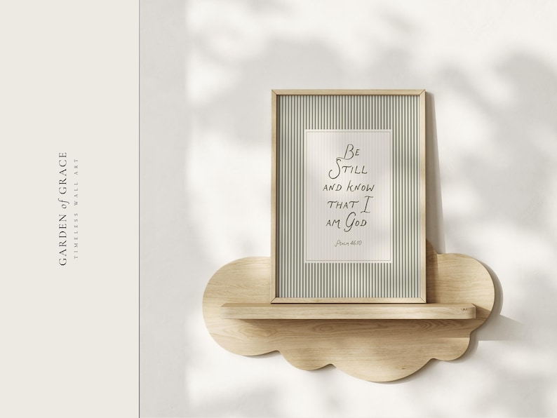 May include: A framed print with the text "Be Still and Know That I Am God" on a striped background, displayed on a cloud-shaped wooden shelf. The frame is light-colored, and the shelf is made of natural wood. The words "Garden of Grace" are on the left.