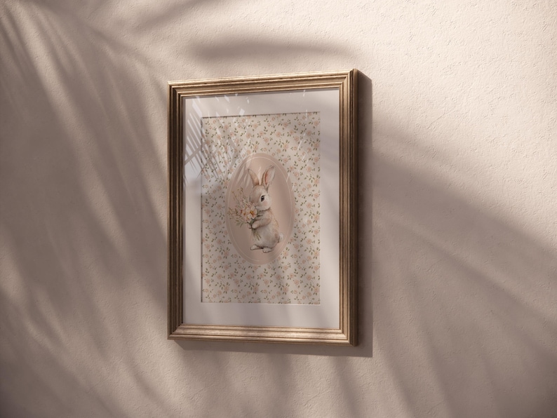 K&ouml;nnte beinhalten: Gerahmtes Kunstwerk mit einer detaillierten Illustration eines Hasen, der Blumen h&auml;lt. Der Hase befindet sich vor einem floralen Hintergrund in einer ovalen Form. Der Rahmen ist hellbraun, und das Kunstwerk h&auml;ngt an einer beigefarbenen Wand.