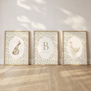 May include: Three framed art prints with a woodland theme. One features a rabbit, another a goose, and the third a letter "B" with the name "Blaire". Each print has a floral background and a light wood frame.