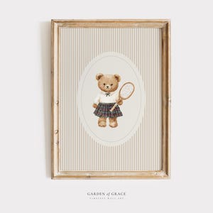 K&ouml;nnte beinhalten: Gerahmter Druck mit einer Aquarellillustration eines Teddyb&auml;ren, der ein wei&szlig;es Hemd und einen karierten Rock tr&auml;gt und einen Tennisschl&auml;ger h&auml;lt. Der Hintergrund hat vertikale beige und wei&szlig;e Streifen. Der Rahmen ist hellbraun.