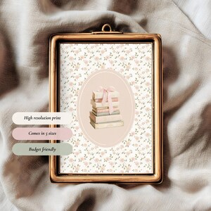 May include: A framed print with a gold-colored frame. The print features a floral pattern background and a central oval with a stack of books tied with a pink ribbon. Text on the image reads: High resolution print, Comes in 5 sizes, Budget friendly.