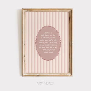 May include: A framed print with a light brown wooden frame. The artwork has a pink and white striped background with an oval design in the centre. The oval contains text in a script font. The words "GARDEN OF GRACE" are at the bottom.