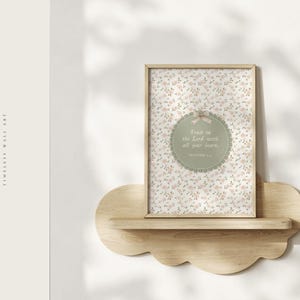 Op de afbeelding: Een ingelijste bloemenprint met de tekst "Trust in the Lord with all your heart" staat op een houten, wolkvormig plankje. De print heeft een lichtbeige achtergrond met kleine roze en witte bloemen.