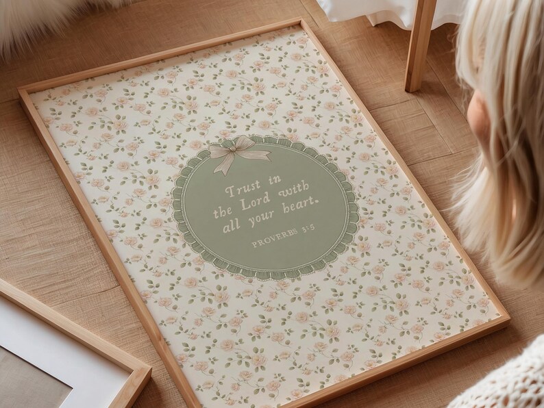 Op de afbeelding: Een ingelijste print met een bloemenpatroon achtergrond en de tekst "Trust in the Lord with all your heart." De print heeft een lichtbruine houten lijst en een decoratief ovaal met een strik.