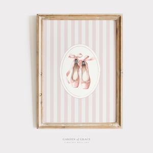 Puede incluir: Arte de pared enmarcado con una ilustración de acuarela de zapatillas de ballet rosas con cintas, sobre un fondo a rayas rosas y blancas. La obra de arte está enmarcada en un marco de madera, con el texto "GARDEN OF GRACE" en la parte inferior.