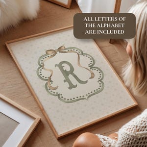 May include: A framed print featuring the letter "R" in a decorative, watercolor style. The letter is in a green hue, set against a cream background with a floral pattern. The frame is light brown, and the text "ALL LETTERS OF THE ALPHABET ARE INCLUDED" is visible.
