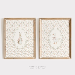 Può includere: Due stampe incorniciate con illustrazioni ad acquerello. Una mostra un coniglio con un cappotto rosa, l'altra un'oca con un fiocco rosa. Entrambe sono ambientate su uno sfondo floreale e incorniciate in legno chiaro.