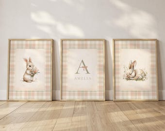 May include: Three framed art prints featuring watercolor illustrations of bunnies. One print shows a bunny holding flowers, another displays the letter "A" with the name "AMELIA", and the third depicts a sleeping bunny. The frames have a plaid pattern.