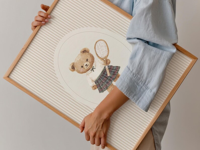 K&ouml;nnte beinhalten: Ein gerahmter Druck mit einer Aquarellillustration eines Teddyb&auml;ren in Tennisbekleidung, der einen Schl&auml;ger h&auml;lt. Der B&auml;r tr&auml;gt ein wei&szlig;es Hemd, einen karierten Rock und eine Fliege. Der Hintergrund hat beige und wei&szlig;e Streifen.