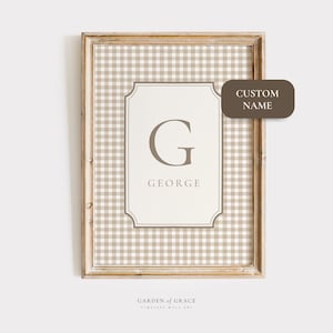 Op de afbeelding: Ingelijste wandkunst met een beige en wit geruit patroon op de achtergrond. Het kunstwerk heeft een wit rechthoekig midden met de letter "G" en de naam "GEORGE" in een schreefletter. Een bruin label leest "CUSTOM NAME".