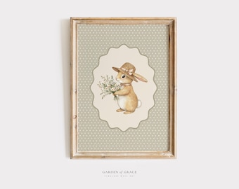 May include: A framed print featuring a watercolor illustration of a bunny wearing a straw hat and holding a bouquet of flowers. The bunny is set against a cream-colored, scalloped background with a dotted pattern, within a wooden frame. The text "GARDEN OF GRACE" is at the bottom.