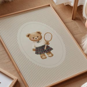K&ouml;nnte beinhalten: Gerahmter Druck mit einer Aquarellillustration eines Teddyb&auml;ren in Tennisbekleidung. Der B&auml;r h&auml;lt einen Tennisschl&auml;ger vor einem gestreiften Hintergrund. Der Rahmen besteht aus hellbraunem Holz, misst ca. 40 x 60 cm.