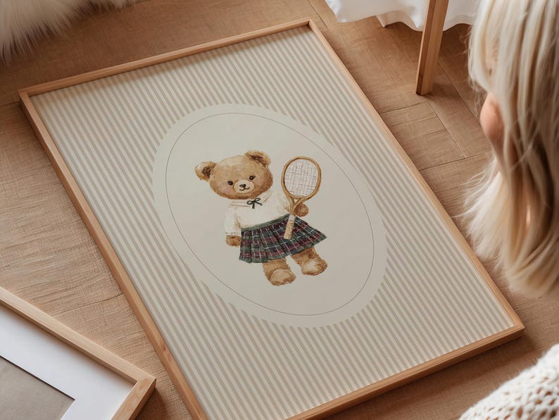 K&ouml;nnte beinhalten: Gerahmter Druck mit einer Aquarellillustration eines Teddyb&auml;ren in Tennisbekleidung. Der B&auml;r h&auml;lt einen Tennisschl&auml;ger vor einem gestreiften Hintergrund. Der Rahmen besteht aus hellbraunem Holz, misst ca. 40 x 60 cm.