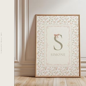 Pu&ograve; includere: Opera d'arte da parete incorniciata con un motivo floreale e un design centrale con il nome "Simone" e la lettera "S". L'opera d'arte ha una combinazione di colori rosa chiaro e verde, con un dettaglio a fiocco sopra la lettera. La cornice &egrave; di colore marrone caldo.