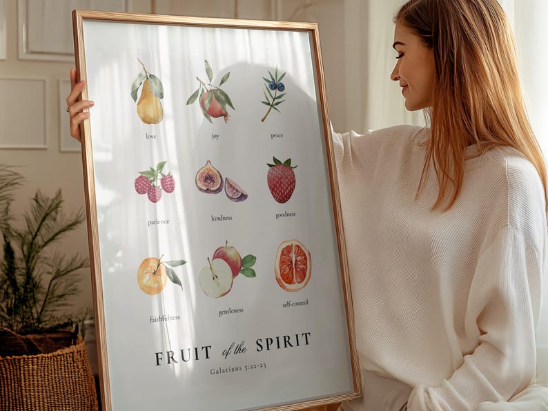 May include: A framed print with a white background and a watercolour illustration of fruits representing the fruit of the spirit. The text "FRUIT of the SPIRIT" is in bold black letters with the scripture reference "Galatians 5:22-23" below. The fruits include a pear, pomegranate, berries, figs, strawberries, apples, and an orange.