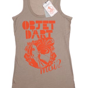 May include: A light brown tank top with a graphic print of a woman's face in a circle with the text "OBJET D'ART moi?" in orange.