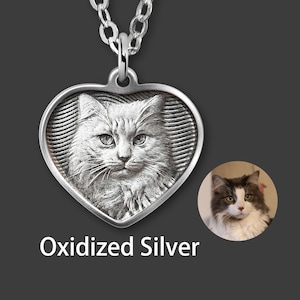 Puede incluir: Collar con colgante en forma de corazón de plata oxidada con un retrato detallado de un gato. La cara del gato está centrada, con un fondo texturizado. Las palabras "Oxidized Silver" se muestran debajo.