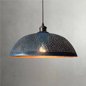 Peut inclure: Un luminaire suspendu bleu en forme de dôme avec un design perforé. L'abat-jour en métal a une finition vieillie et un intérieur doré et chaleureux. La lumière est suspendue à un cordon et un luminaire noirs, créant une esthétique industrielle vintage.