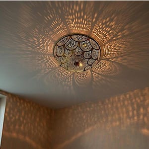 May include: A decorative ceiling light fitting with a patterned design. The light casts intricate shadows on the ceiling and walls. The fitting is round with a detailed, openwork pattern, creating a warm, inviting ambience.