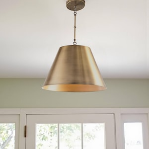 May include: A brass-toned pendant light fixture with a conical shade. The light hangs from a chain and ceiling mount. The shade has a warm, inviting glow. This fixture is suitable for a kitchen or dining room.