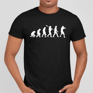 May include: Black t-shirt featuring a white graphic of the evolution of man, culminating in a boxer. The design shows a progression from ape-like figures to a person in boxing stance. The shirt is a classic crew neck.