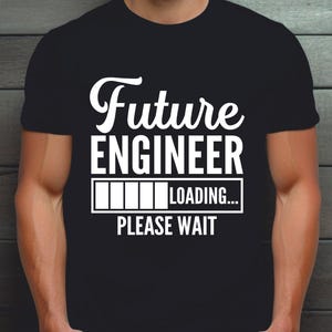 Puede incluir: Una camiseta negra de manga corta con texto blanco que dice Future ENGINEER, un gráfico de una barra de carga y el texto LOADING... PLEASE WAIT centrado en el pecho. El diseño está impreso en una fuente negrita, clara y sin remates.
