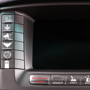May include: A black dashboard with a large screen and several buttons. The buttons have white icons and text, including "Self-Destruct Sequence", "Invisibility", "Eject", "Siren", "Target Lock", and "Missile Launch".
