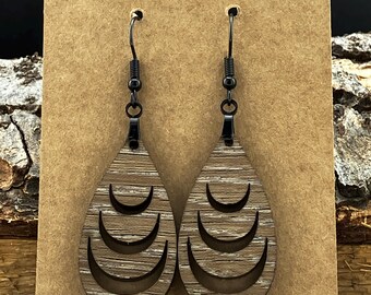 May include: A pair of wooden teardrop earrings with a layered crescent moon design. The earrings are brown with a wood grain pattern and have black metal hooks.