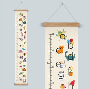 May include: A cream-coloured height chart with wooden accents, featuring a colourful alphabet and whimsical illustrations. The chart measures up to 170 cm and is designed for children's rooms.