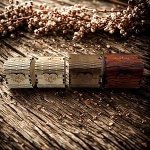 Könnte beinhalten: Vier kleine Ringboxen aus Holz mit Herz- und dekorativen Designs. Die Boxen sind in verschiedenen Brauntönen gehalten, eine Box trägt das Wort "wedding". Die Boxen sind auf einer rustikalen Holzoberfläche angeordnet.