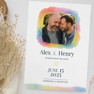 May include: Wedding invitation with a photo of two men, set within a watercolour rainbow border. Text reads "Alex & Henry, Please Save the Date, June 15, 2025, Ceremony & Reception."